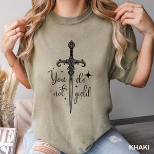 Peut inclure: T-shirt kaki avec un motif d'&eacute;p&eacute;e noire et l'inscription &laquo; You do not yield &raquo;. Le graphisme comprend des &eacute;toiles et des ornements d&eacute;coratifs. Le t-shirt est de couleur neutre et &agrave; manches courtes.