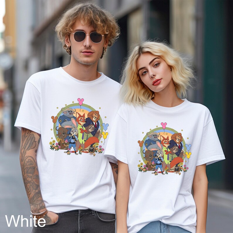 Pode incluir: T-shirts brancas com um gr&aacute;fico de desenho animado colorido de personagens de animais. O gr&aacute;fico inclui uma raposa, um coelho e outros animais em um design circular com flores e bal&otilde;es. A palavra "White" &eacute; impressa na parte inferior.