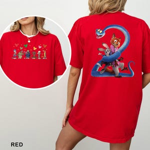 K&ouml;nnte beinhalten: Rotes T-Shirt mit Cartoon-Illustrationen. Auf der Vorderseite sind Cartoon-Figuren mit herzf&ouml;rmigen Luftballons abgebildet. Auf der R&uuml;ckseite ist eine blaue Schlange um einen Fuchs und ein Kaninchen gewickelt.