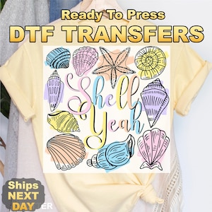 May include: A light yellow t-shirt featuring a colorful seashell design with the words "Shell Yeah". The design includes various seashells and a starfish in pastel colors. The text "Ready To Press DTF TRANSFERS" is at the top.