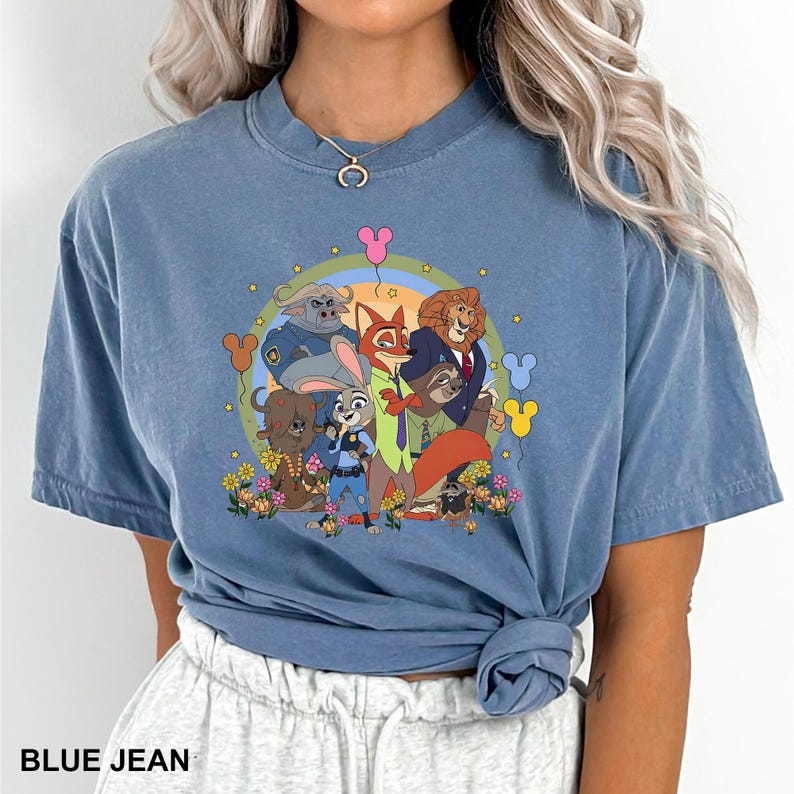 Pode incluir: Camiseta azul jeans com um gr&aacute;fico de desenho animado colorido de personagens de um filme de anima&ccedil;&atilde;o popular. O gr&aacute;fico inclui um arco-&iacute;ris, flores e bal&otilde;es. O texto "BLUE JEAN" &eacute; impresso na parte inferior da camiseta.