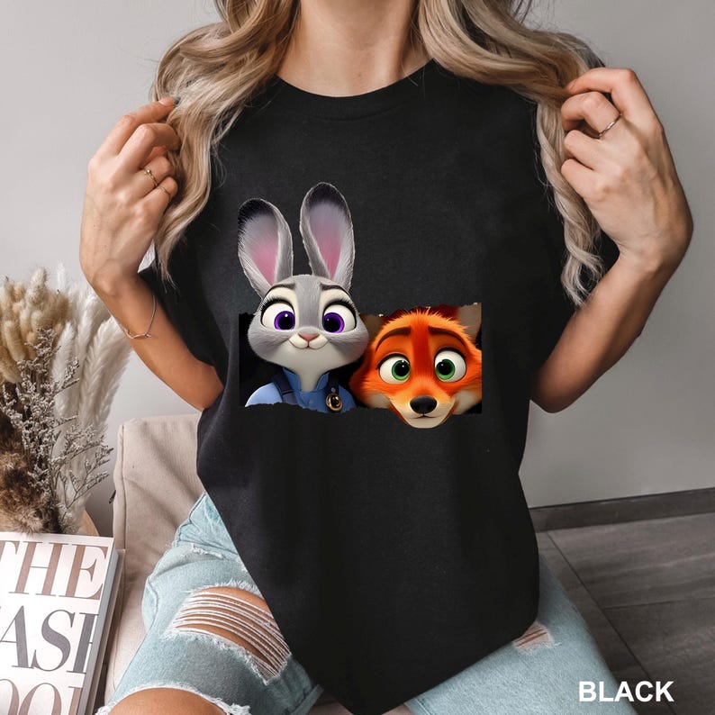 May include: Black t-shirt featuring a graphic of Judy Hopps and Nick Wilde from Zootopia. The cartoon characters are in a pocket-like design. The word "BLACK" is printed at the bottom right.