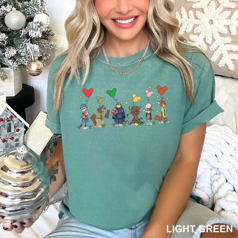 May include: Light green t-shirt with a cartoon animal design, including a bunny, bear, and fox, each holding a balloon. The text "LIGHT GREEN" is at the bottom of the image. The t-shirt is a relaxed fit.