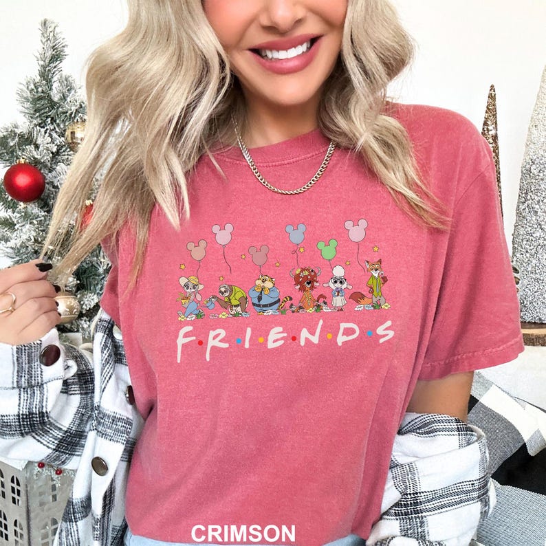 May include: Crimson-colored t-shirt featuring a cartoon design of animal characters holding Mickey Mouse balloons above the word "FRIENDS". The shirt has a crew neck and short sleeves. The word "CRIMSON" is printed at the bottom of the shirt.