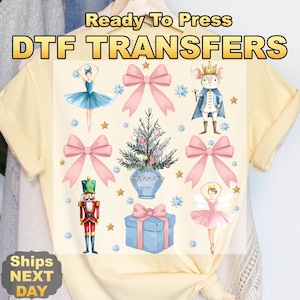 May include: A light yellow t-shirt featuring a DTF transfer print with a ballerina, a nutcracker, a mouse prince, a Christmas tree, a gift box, and pink bows. The text reads Ready To Press DTF TRANSFERS and Ships NEXT DAY.