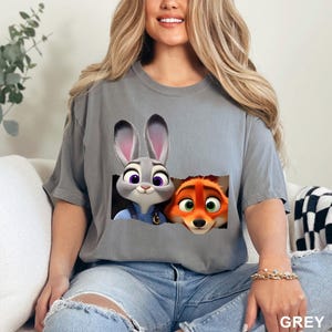 May include: Grey t-shirt featuring Judy Hopps and Nick Wilde from Zootopia. The graphic shows the characters peeking out from a torn-paper effect. The word "GREY" is printed in the bottom right corner of the image.