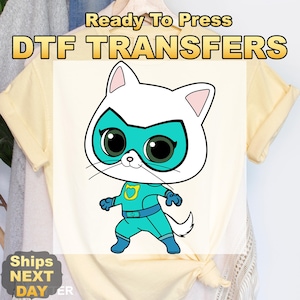 May include: DTF transfer featuring a cartoon cat superhero in a teal and white costume. The cat has large green eyes and a white mask. The text "Ready To Press DTF TRANSFERS" is at the top. The words "Ships Next Day" are at the bottom.