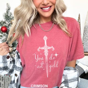 Peut inclure: T-shirt de couleur cramoisie avec une &eacute;p&eacute;e blanche et le texte "You do not yield". Le t-shirt a des manches courtes et un col rond. Le mot "CRIMSON" est imprim&eacute; en bas du t-shirt.