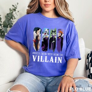 Puede incluir: Camiseta azul con cuatro villanos de dibujos animados y el texto "Sweetie I'm OK with Being the Villain". La camiseta es de color azul liso y tiene un corte holgado.