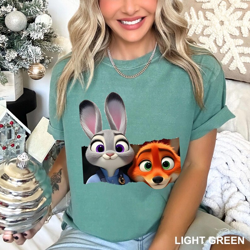 May include: Light green t-shirt featuring a graphic of Judy Hopps and Nick Wilde from Zootopia. The characters are depicted in a rectangular cutout. The text "LIGHT GREEN" is printed at the bottom of the shirt.