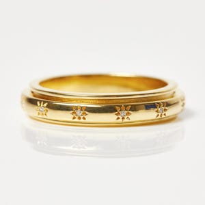 Könnte beinhalten: Ein goldfarbener Ring mit floralem Design. Der Ring weist kleine, funkelnde Akzente innerhalb der floralen Muster auf. Der Ring ist vor einem weißen Hintergrund platziert, der seine komplizierten Details hervorhebt.