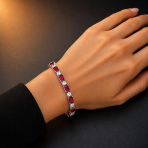 May include: A silver-toned tennis bracelet featuring alternating rectangular-cut deep red rubies and square-cut clear white stones. The bracelet is constructed with a linked metal setting that secures each gemstone in a repeating pattern.