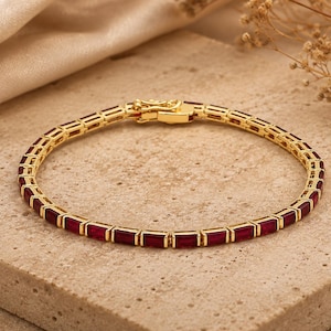 Könnte beinhalten: Ein goldfarbenes Armband mit rechteckigen, tiefroten Edelsteinen. Das Armband liegt auf einer neutralen Oberfläche, mit einem Verschluss oben. Die Edelsteine sind gleichmäßig angeordnet. Das Armband ist etwa 18 cm lang.