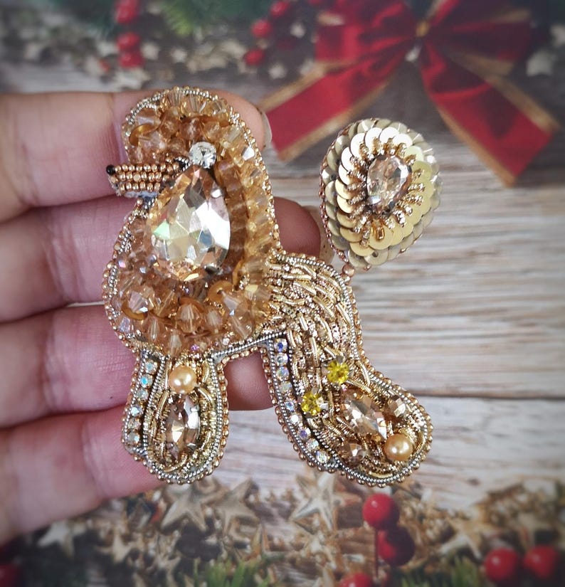 May include: A gold-toned, beaded poodle brooch with a large, teardrop-shaped crystal pendant. The brooch features intricate beadwork, sequins, and smaller crystals, creating a sparkling, three-dimensional effect. The poodle's tail is a circular cluster of gold sequins.