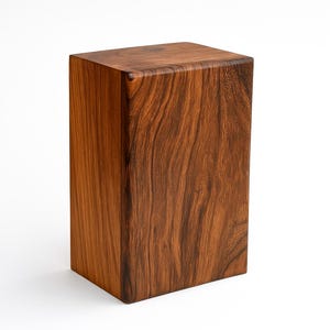 Op de afbeelding: Een massief, rechthoekig houten blok met een diepbruine kleur en zichtbare houtnerf. De eenvoudige, geometrische vorm suggereert een decoratief of functioneel gebruik, mogelijk als kleine standaard. De natuurlijke textuur van het hout is duidelijk zichtbaar.