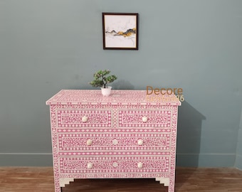 May include: A pink and white floral patterned chest of drawers with four drawers and white knobs. The chest is made of wood and has a decorative design. A small plant in a white pot sits on top of the chest.