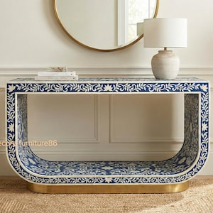 May include: A blue and white patterned console table with a gold base. The table features a curved design and is decorated with floral patterns. A lamp and books sit on top of the table. The table is 60 inches long.