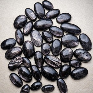 Puede incluir: Colección de piedras preciosas negras pulidas, de forma ovalada, con brillo metálico. Las piedras varían en tamaño y están dispuestas juntas, creando una exhibición visualmente atractiva. Las piedras tienen una superficie lisa y reflectante.