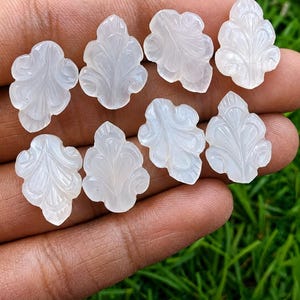 May include: Eight translucent white gemstones carved into leaf shapes with intricate vein detailing. Each piece features a smooth, polished surface and a symmetrical design, showcasing a soft glow and a distinct, organic, botanical-inspired silhouette.