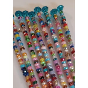 May include: A collection of colorful beaded hair sticks. Each stick features a variety of beads in shades of blue, pink, yellow, green, and more. The tops of the sticks are adorned with faceted blue crystal-like beads.