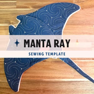 Op de afbeelding: Een mantarog-naaipatroon van donkerblauwe stof met een wit wervelend stippenpatroon. De vorm is plat en breed met een lange, puntige staart. De tekst MANTA RAY SEWING TEMPLATE is in het zwart in het midden van het object gedrukt.