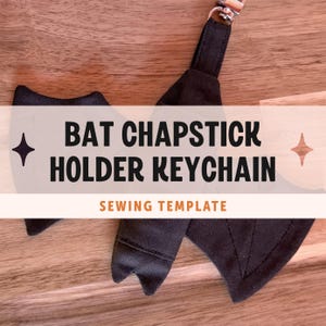 May include: A black fabric bat-shaped chapstick holder keychain with stitched wing details and a silver metal swivel clasp. The text BAT CHAPSTICK HOLDER KEYCHAIN SEWING TEMPLATE is overlaid on the image in black and orange lettering.