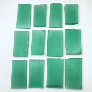 May include: Eleven rectangular pieces of translucent green glass arranged in three rows. Each piece features a smooth, flat surface with subtle variations in tone and texture, showcasing a consistent rectangular shape and a soft, matte finish.