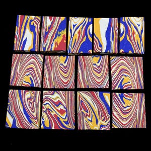May include: A collection of twelve rectangular blocks featuring a marbled pattern in vibrant shades of blue, red, yellow, and white. Each block displays unique swirling lines and organic colour distributions across its flat surface.