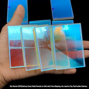 May include: A collection of rectangular glass tiles featuring a vibrant iridescent finish that shifts between shades of bright blue, cyan, and subtle yellow highlights. The smooth, reflective surfaces catch the light, creating a luminous effect.
