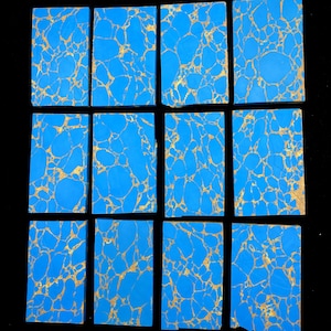 May include: Twelve rectangular slabs of bright blue material featuring a complex, web-like pattern of thin, metallic gold veins running throughout each piece. The slabs are arranged in a grid of three rows and four columns against a black background.