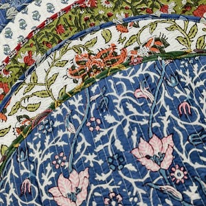 Könnte beinhalten: Ein Stapel runder, gesteppter Stoff-Platzsets mit verschiedenen Blumenmustern in Blau, Grün, Weiß, Orange und Rosa. Jedes Stück zeigt einen botanischen Druck mit komplexen Ranken- und Blumenmotiven und ist mit einer abgesteppten Kante versehen.