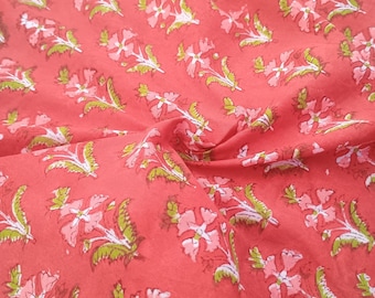 Può includere: Primo piano di un tessuto color corallo con un motivo floreale ripetuto. Il design presenta fiori rosa e bianchi con foglie verdi. Il tessuto è leggermente stropicciato, aggiungendo consistenza all'immagine.