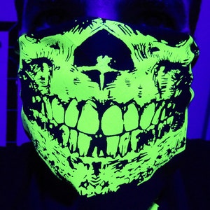 May include: A green and black skull face mask with a wide grin. The mask is made of a soft, flexible material and is designed to cover the nose and mouth.