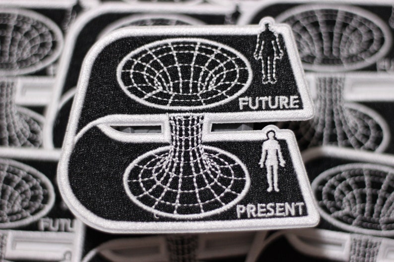 May include: Black and white embroidered patch with a stylized image of a wormhole. The patch has the words "FUTURE" and "PRESENT" on it.