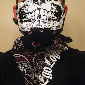 May include: A black bandana with a paisley pattern and white text that reads "Cool Dog" is worn around the neck of a person wearing a skull-printed face mask.