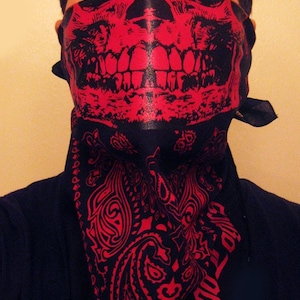 Op de afbeelding: Een persoon draagt ​​een zwarte bandana met een rood schedel- en kruisbeenderontwerp. De bandana heeft een paisley-patroon aan de onderkant.