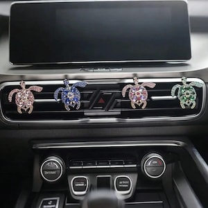 May include: Four bejeweled turtle car vent clips in pink, blue, purple, and green. Each turtle is encrusted with sparkling rhinestones. The clips are attached to the car's air vent, adding a decorative touch to the vehicle's interior.