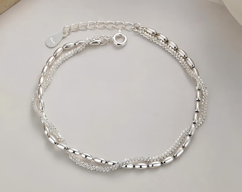 May include: A silver bracelet with two strands. One strand features small, oval beads, while the other has a delicate, textured design. The bracelet has a lobster clasp closure and an adjustable chain. The word "ORPHIQUE JEWELLERY" is printed at the bottom.