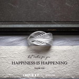 Puede incluir: Un anillo plateado con un dise&ntilde;o tejido, sobre una superficie blanca texturizada. El anillo presenta un patr&oacute;n complejo de hebras de metal entrelazadas. El texto "best wishes for you HAPPINESS IS HAPPENING THANK YOU" es visible.