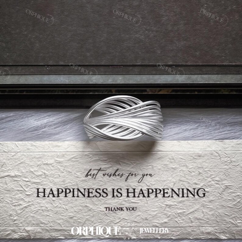 Puede incluir: Un anillo plateado con un dise&ntilde;o tejido, sobre una superficie blanca texturizada. El anillo presenta un patr&oacute;n complejo de hebras de metal entrelazadas. El texto "best wishes for you HAPPINESS IS HAPPENING THANK YOU" es visible.