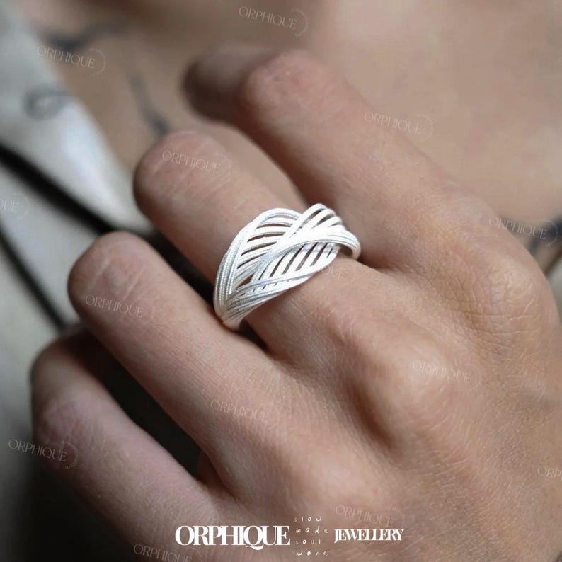 Puede incluir: Un anillo de plata con un dise&ntilde;o de hoja tejida. El anillo presenta una serie de l&iacute;neas paralelas que crean un patr&oacute;n calado texturizado. El anillo se lleva en un dedo, y la est&eacute;tica general es moderna y elegante. El anillo es de la marca ORPHIQUE JEWELLERY.