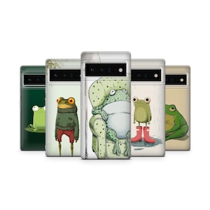 May include: A collection of phone cases featuring whimsical frog illustrations. Each case showcases a different frog design, including one in a sweater, another in rain boots, and one relaxing in a chair. The cases are in various colors, including green, beige, and white.