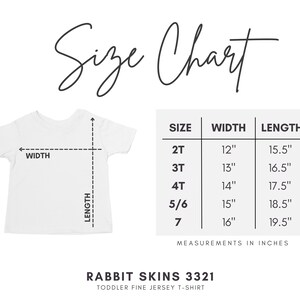 May include: A white toddler t-shirt with a size chart. The chart shows measurements in inches for sizes 2T to 7, including width and length. The text "Size Chart" is at the top, and "Rabbit Skins 3321 Toddler Fine Jersey T-Shirt" is at the bottom.