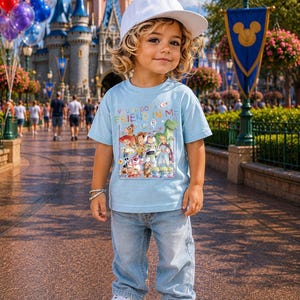 May include: A young child wearing a light blue t-shirt with a graphic of Toy Story characters and the text "You've Got a Friend in Me." The child is also wearing light blue jeans, white sneakers, and a white baseball cap. The background includes a castle and balloons.