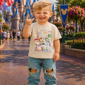 May include: A young child wearing a beige t-shirt with the text "You've Got a Friend in Me" and a graphic of Toy Story characters. The child is also wearing ripped blue jeans and white sneakers, smiling and making a hand gesture.