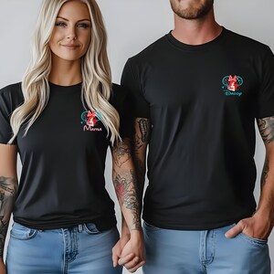 May include: Two black short-sleeved t-shirts featuring a small graphic on the left chest. The graphic depicts a red-bowed character with the text Mama on one shirt and Daddy on the other, paired with light blue denim jeans.