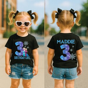 K&ouml;nnte beinhalten: Ein schwarzes T-Shirt mit einer blau-violetten Zahl 3 und einem Schneeflocken-Design. Auf der Vorderseite des Shirts steht "BIRTHDAY GIRL" und zeigt eine Grafik von zwei Charakteren. Auf der R&uuml;ckseite des Shirts steht "MADDIE" und hat eine 3.