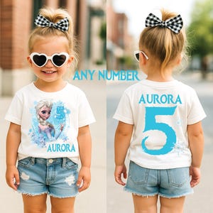 Pu&ograve; includere: Maglietta bianca con grafica di personaggio dei cartoni animati e il numero 5 in blu. Il nome "Aurora" &egrave; stampato sul davanti e sul retro. &Egrave; visibile anche il testo "ANY NUMBER".