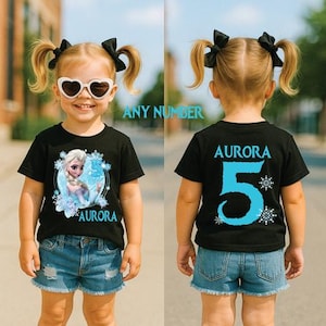 Pu&ograve; includere: T-shirt nero con grafica di una principessa dei cartoni animati e il numero 5 in blu. La parte anteriore della maglietta dice "Aurora" e il retro "Aurora 5". La maglietta &egrave; indossata da una bambina con le trecce e gli occhiali da sole.
