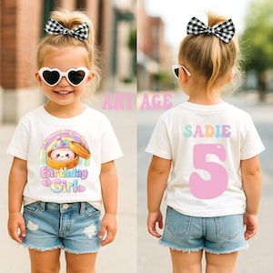 May include: A white t-shirt featuring a graphic of a dumpling in a bamboo steamer with a party hat under a rainbow and the text Birthday Girl on the front, and the name SADIE with the number 5 in large pink font on the back.